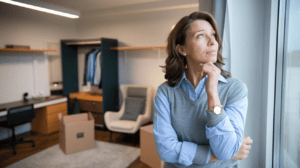 Ja-Sagen eine ca. 45-jährige Europäerin steht im Raum ihres Kindes, das gerade das Nest verlässt. Es stehen noch einige Umzugskartons, ein Sessel und ein Kleiderschrank in dem einige Kleidungsstücke hängen im sonst leeren Raum.